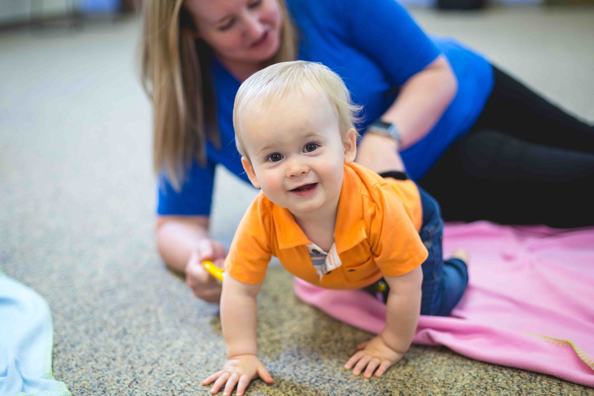 A smiling baby moving and playing with their mom in a Kindermusik foundations class.