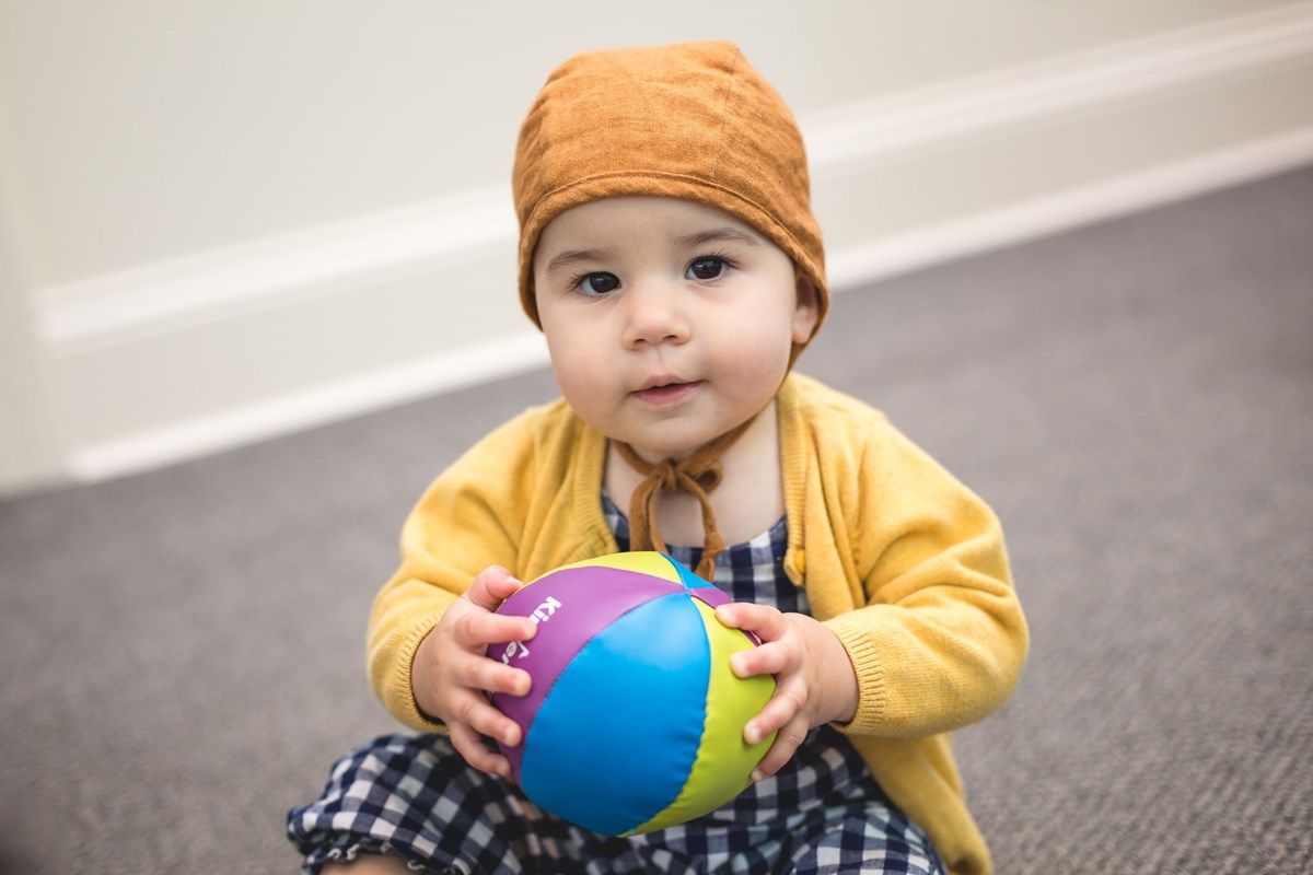 Baby gripping a soft chime ball. What you’ll learn in a music class for babies and infants