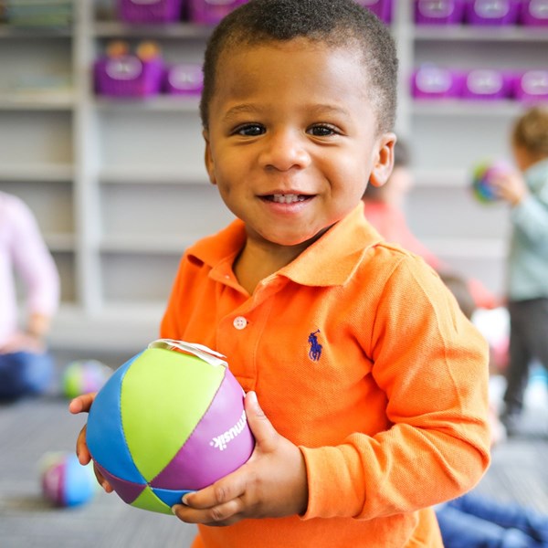 2-year-old boy plays with a soft chime ball during music classes for older toddlers.